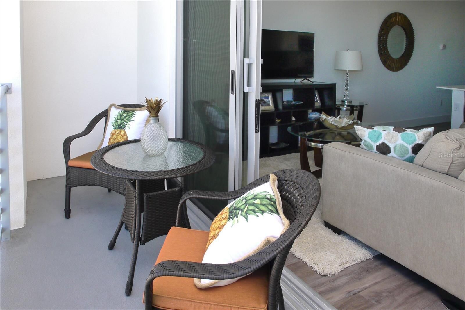 A living room with a sofa, two wicker chairs, a glass-top table, a television, and a decorative mirror.