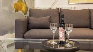 A bottle of wine on a tray with two glasses on a glass table in a living room with a grey sofa and a map on the wall. - Spacious 4 bedroom Apartment near St. Peter's Basilica (Roma)