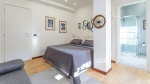 A bedroom with a bed, a gray sofa, and a shower area visible through an open door. - Spacious 4 bedroom Apartment near St. Peter's Basilica (Roma)