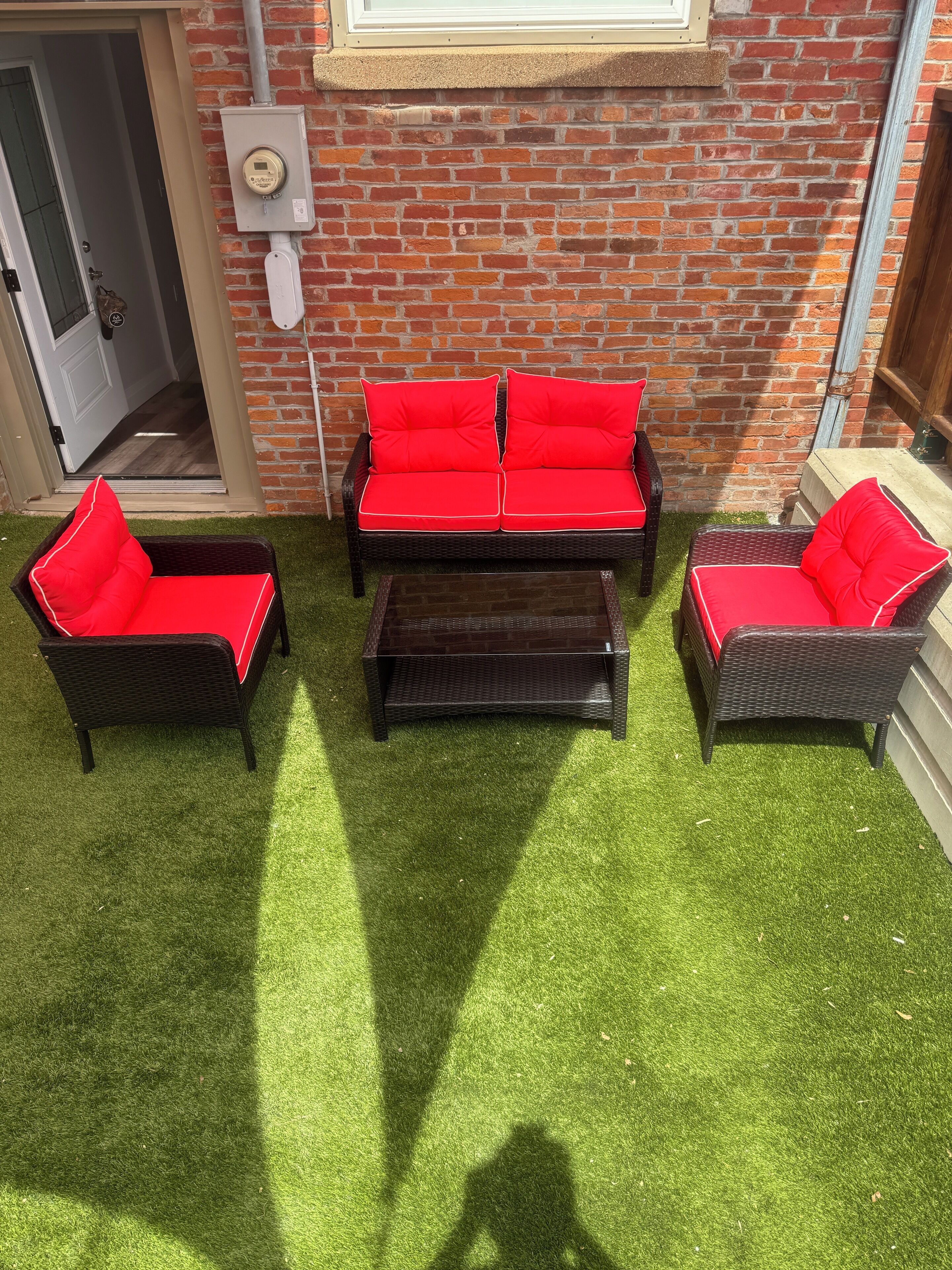 Un patio con un muro de ladrillo, un juego de sofá rojo y una pequeña mesa.