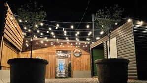 Un espace extérieur doté d’une entrée en bois, de guirlandes lumineuses et de deux grands jardinières.
