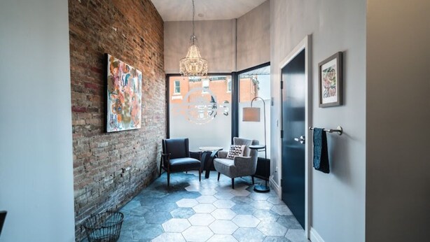 Un couloir moderne avec un mur en briques, un sol à motifs hexagonaux, deux fauteuils, un lustre et des œuvres d’art.