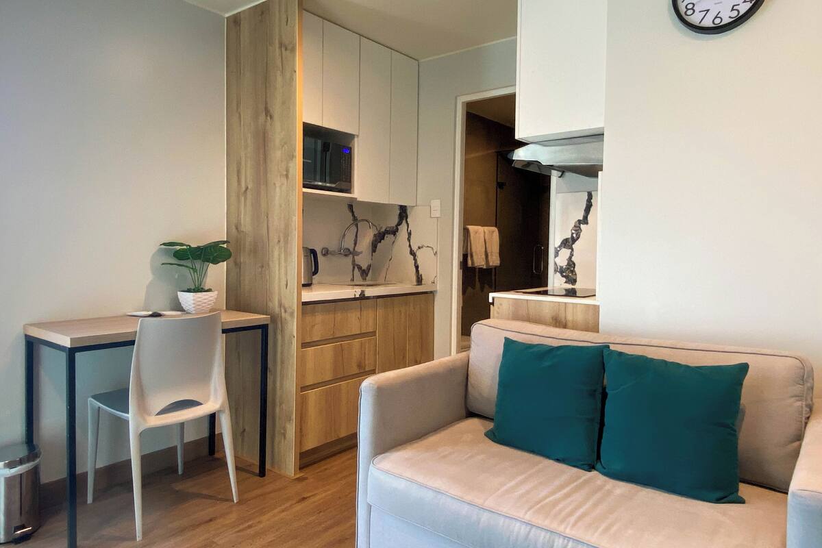 Un salon moderne avec un canapé, un coin repas comprenant une chaise et une table, et une cuisine équipée d’un four à micro-ondes.