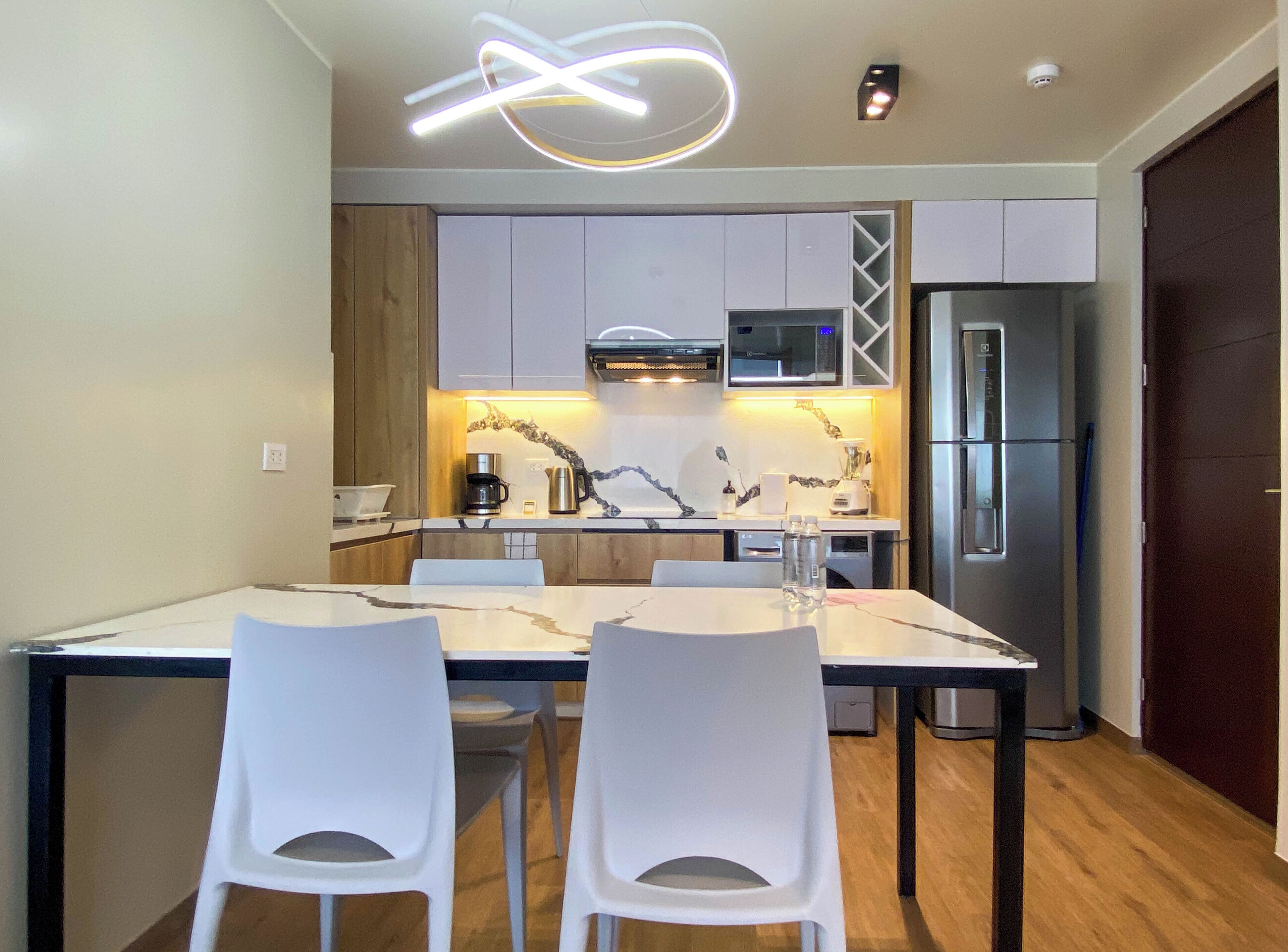 A modern kitchen with white cabinets, a stainless steel refrigerator, and a dining area with two white chairs.