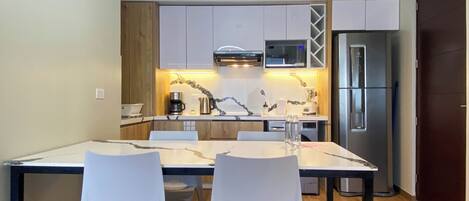A modern kitchen with white cabinets, a stainless steel refrigerator, and a dining area with two white chairs.