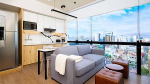 A modern living room with a grey sofa, a small table, and a coffee table. A city view is visible through large windows.