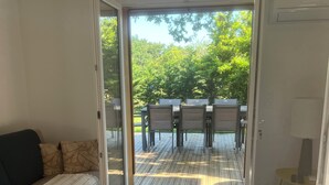 A room with a sofa, a rug, and an open door leading to an outdoor patio with a table and chairs. - Location Atypique Dans un Airial Landais (Mimizan)