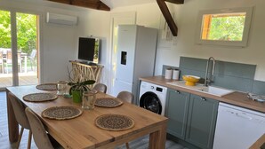 A compact kitchen with a washing machine, a sink, and a dining area with a wooden table and chairs. - Location Atypique Dans un Airial Landais (Mimizan)