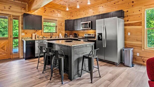 Una cocina moderna con paredes de madera, una isla central con taburetes de bar, electrodomésticos de acero inoxidable y vistas a zonas verdes.