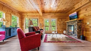 Un interior de cabaña acogedor con chimenea de piedra, paredes de madera y un sillón rojo.