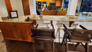 Cocina con armarios de madera, encimeras de granito, un tazón de acero inoxidable y una barra con taburetes.