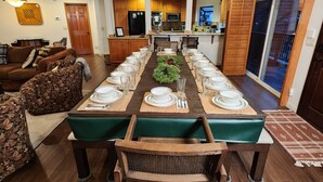 Comedor con una larga mesa lista para una comida, pisos de madera y vistas a la cocina y la sala de estar.