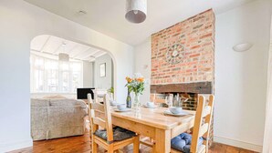 A dining area with a brick fireplace, wooden dining table, and chairs. - Harvest Moon - cottage close to harbour (Weymouth)