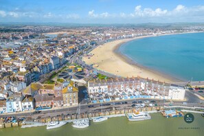 A coastal town with a sandy beach, a marina with boats, and a row of terraced houses along the waterfront. - Harvest Moon - cottage close to harbour (Weymouth)