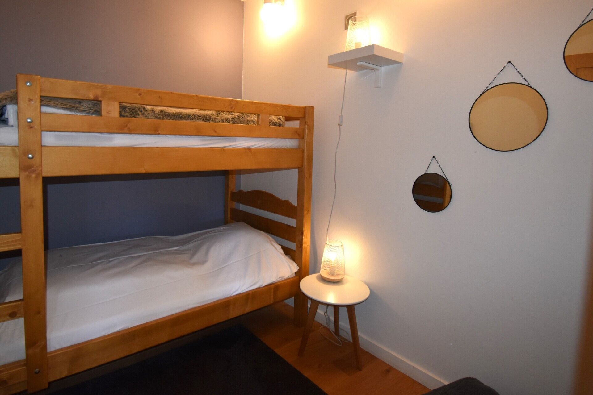 Une chambre avec un lit superposé, un petit tabouret et des lampes fixées au mur.