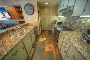 Una cocina con encimeras de granito, refrigerador de acero inoxidable y microondas.
