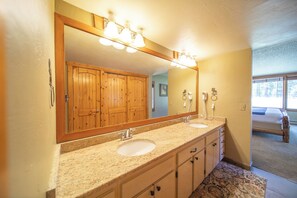Un baño con dos lavamanos, armarios de madera, un espejo grande y una ventana.