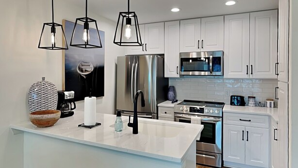 A modern kitchen with white cabinetry, stainless steel appliances, and pendant lighting. - Changes in Attitudes by Miss Kitty’s (Rockport)