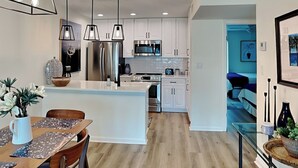 A modern kitchen with white cabinets, stainless steel appliances, and pendant lighting. - Changes in Attitudes by Miss Kitty’s (Rockport)