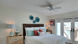 A bedroom with a bed, two bedside tables, a ceiling fan, a view of the outside, and a door to the balcony. - Changes in Attitudes by Miss Kitty’s (Rockport)