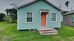 A small, single-story house with a green exterior and a brown front door. - Coral Cottage by Miss Kitty’s (Rockport)