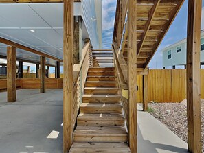 A wooden staircase leading to a covered area with a view of a residential building in the background. - Wash Away the Blues by Silver Sands Vacation Rentals (Port Aransas)