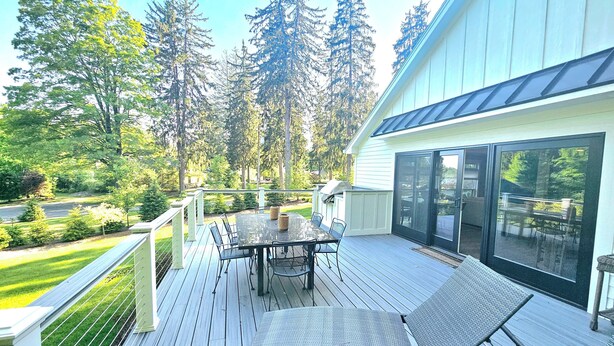 A deck with a table and chairs, surrounded by a railing, overlooking a garden and tall trees. - Newly remodeled, private Villa in Bolton Landing with all the comforts of home (Bolton)