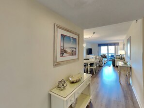 A hallway with a dining area, a living room with a sofa and chairs, and a view of the ocean. - Ketch Court 893 by Hilton Head Retreats (Hilton Head Island)