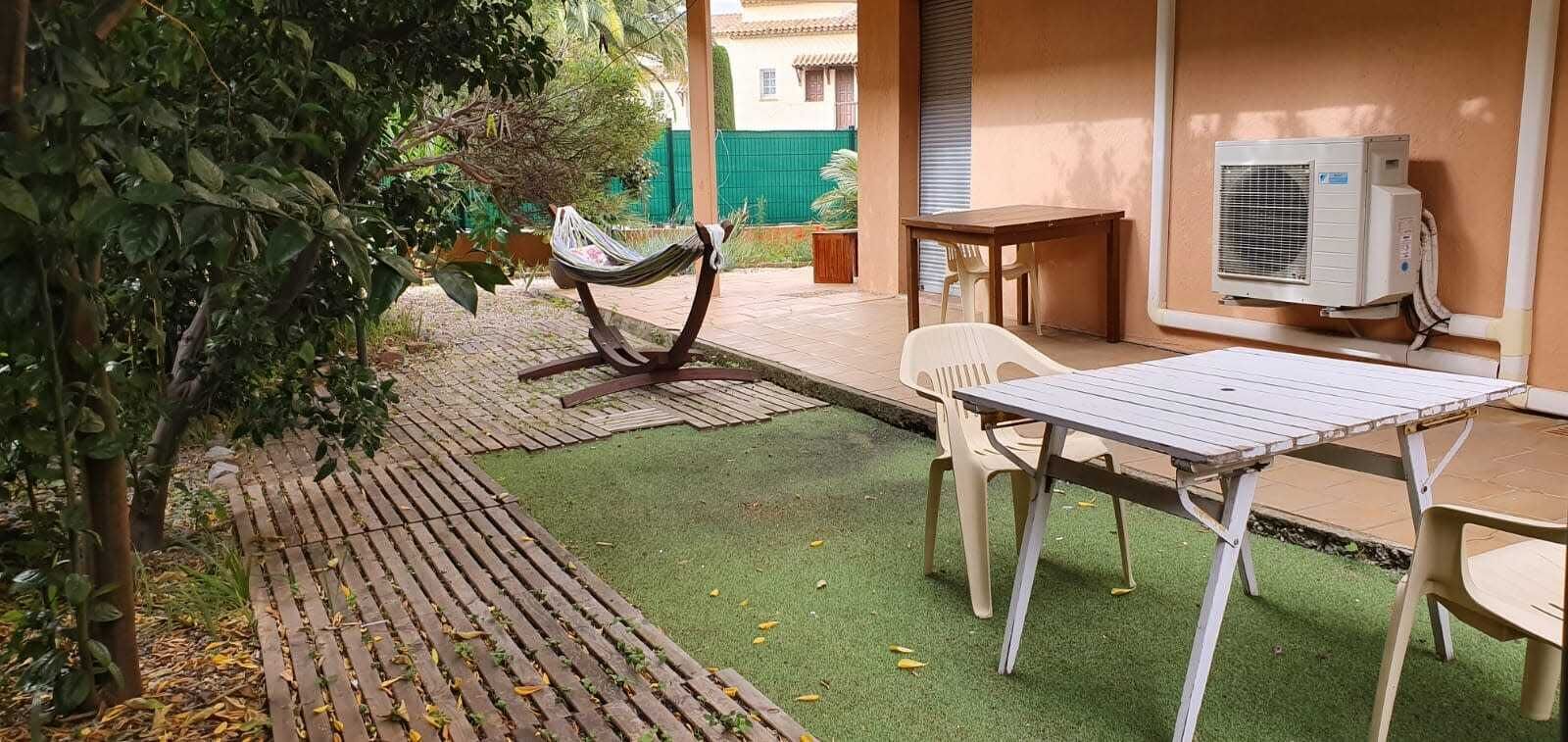 Um pátio externo com uma rede, uma mesa, cadeiras e um aparelho de ar condicionado.