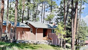 A single-story cabin with a sloped roof, surrounded by tall pine trees. - The Bungalow by Ruidoso Vacation Rentals (Ruidoso)