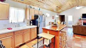 A spacious kitchen with wooden cabinets, a central island, and a dining area with a couch. - The Bungalow by Ruidoso Vacation Rentals (Ruidoso)