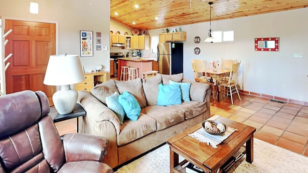 A cozy living room with a brown leather sofa, a wooden coffee table, and a dining area with a wooden table and chairs. - The Bungalow by Ruidoso Vacation Rentals (Ruidoso)