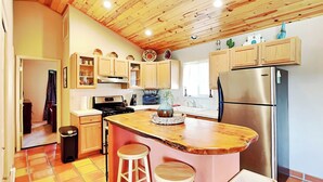 A kitchen with wooden cabinets, a stainless steel refrigerator, a wooden island with stools, and a tiled floor. - The Bungalow by Ruidoso Vacation Rentals (Ruidoso)