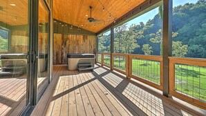 A wooden deck with a glass enclosure, outdoor grill, and a view of a forested area.