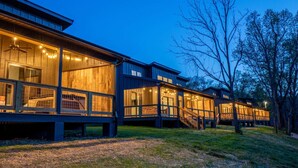 A modern wooden cabin with large windows, a deck, and a staircase leading to the upper level.