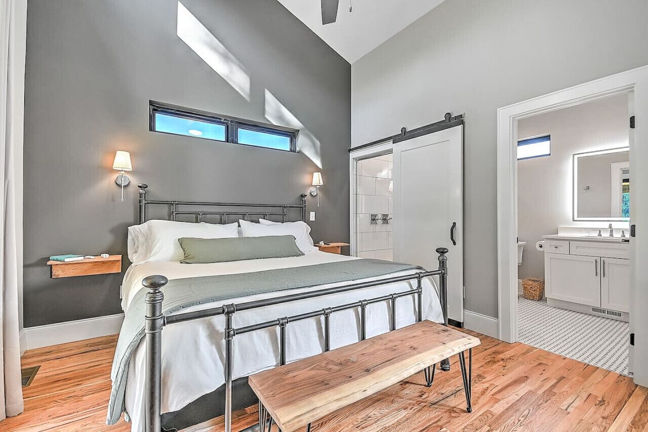 Ein Schlafzimmer mit Bett, Nachttischen, einer Bank, einem Kleiderschrank und einem Badezimmer mit Spiegel und Waschbecken.