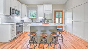 A modern kitchen with white cabinetry, a central island with stools, a microwave, and a refrigerator.