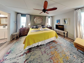 A bedroom with a bed, a ceiling fan, a television, and a painting on the wall. - Beachfront Bliss Bermuda by Ryson Vacation Rentals (Galveston)