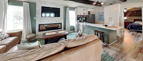 A modern living room with a fireplace, a sofa, a coffee table, and a kitchen area with a bar.