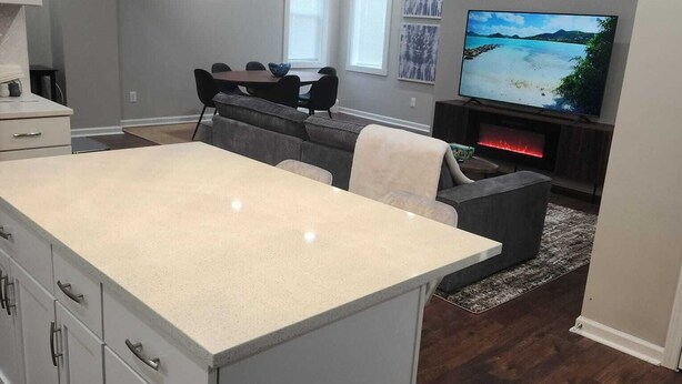 Ein modernes Wohnzimmer mit einer großen Kochinsel, dunklem Holzboden und einem flachbildfernseher an der Wand.
