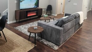 Ein modernes Wohnzimmer mit Kamin, großem Flachbildfernseher, grauem Ecksofa und Couchtisch.