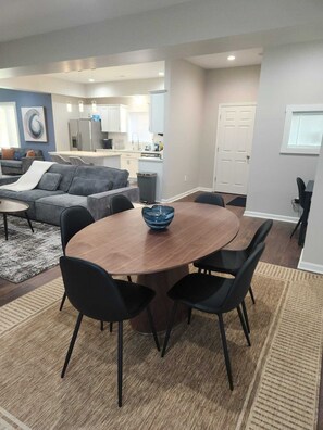 A modern living room with a round wooden table, black chairs, a grey sofa, and a kitchen in the background. - Cozy 3-bedroom house near Lucas Oil Stadium in downtown Indianapolis.  (Indianapolis)