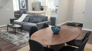 Ein modernes Wohnzimmer mit grauem Sofa, Couchtisch und Essbereich mit Holztisch und schwarzen Stühlen.