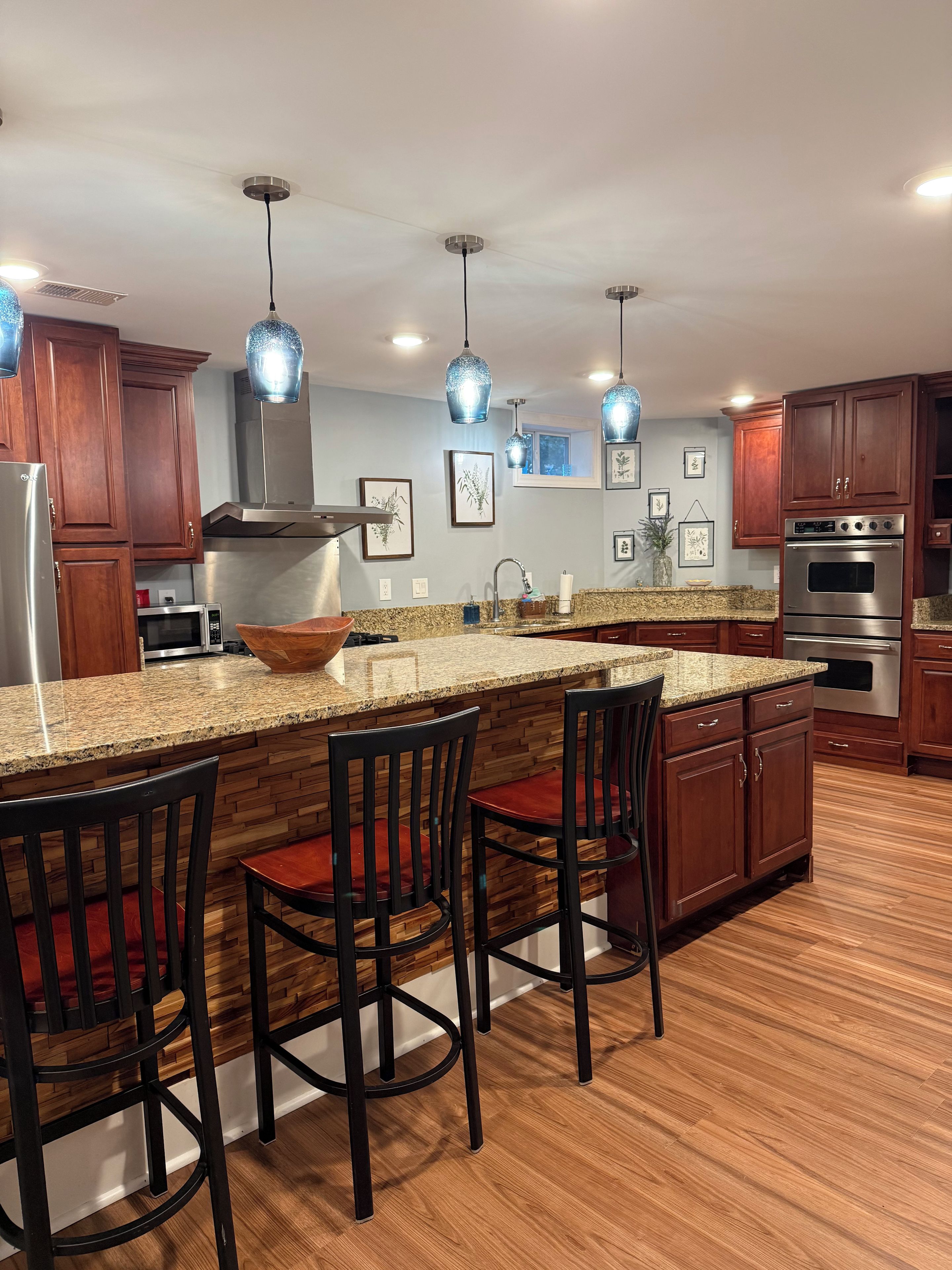 A kitchen with a granite countertop, wooden cabinets, stainless steel appliances, and pendant lighting.