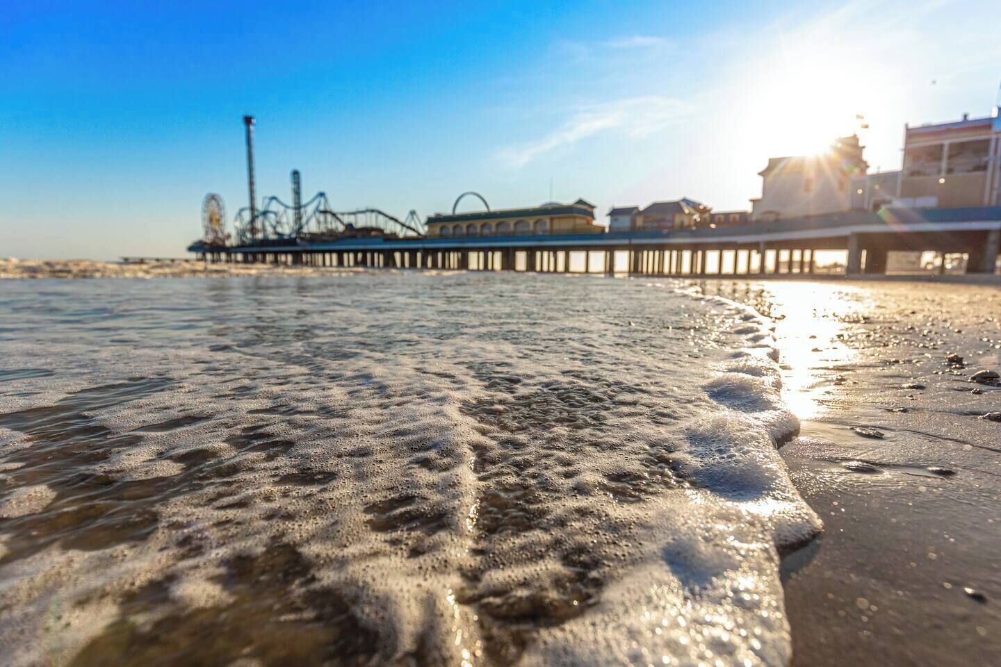 A beach with waves and a pier in the background.