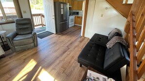 A compact living space with a kitchenette, a sofa, a recliner, and a staircase. - Peaceful Acres Cabin 2 - Eagle's Nest  (Soldotna)