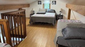 A bedroom with a loft-style ceiling, a bed with grey bedding, two bedside tables with lamps, and a window with curtains. - Peaceful Acres Cabin 3 - Cozy Cottage  (Soldotna)
