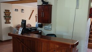 Un mostrador de recepción de madera con una computadora, un letrero que indica disponibilidad de WiFi y un gabinete fijado a la pared.