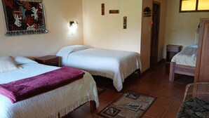 Una habitación con dos camas, una mesita de noche de madera, una pequeña mesa, una silla de mimbre y un adorno colgante en la pared.