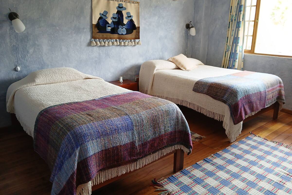 Una habitación con dos camas, un tapiz en la pared y una ventana con cortinas.